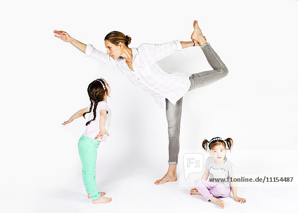 Mutter übt Yoga mit verspielten Töchtern