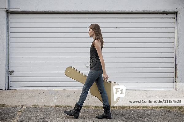 Caucasian woman carrying guitar case on sidewalk
