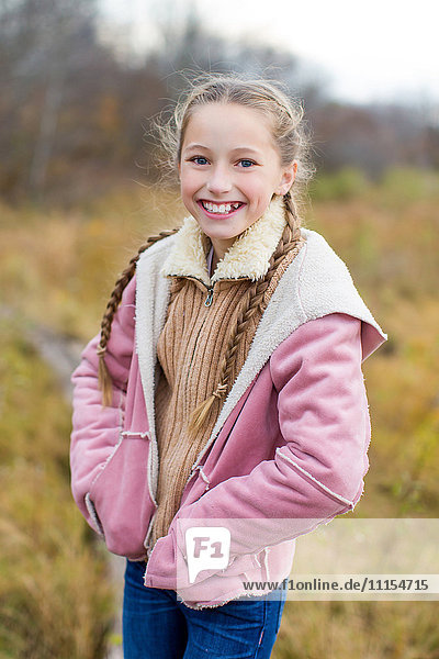 Smiling girl standing with hands in pockets in field