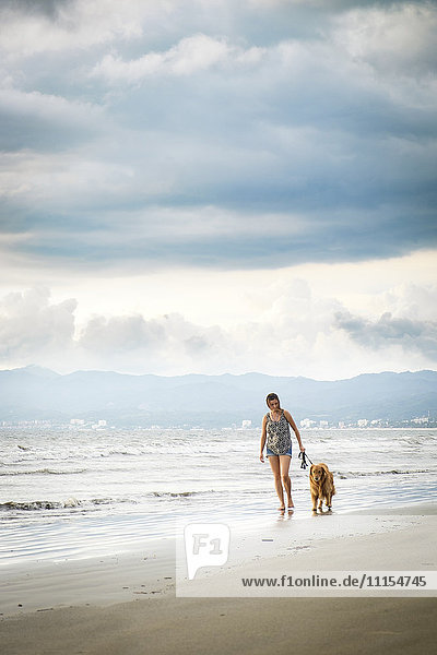 Mexico  Nayarit  Young woman walking Golden Retriever dog at the beach