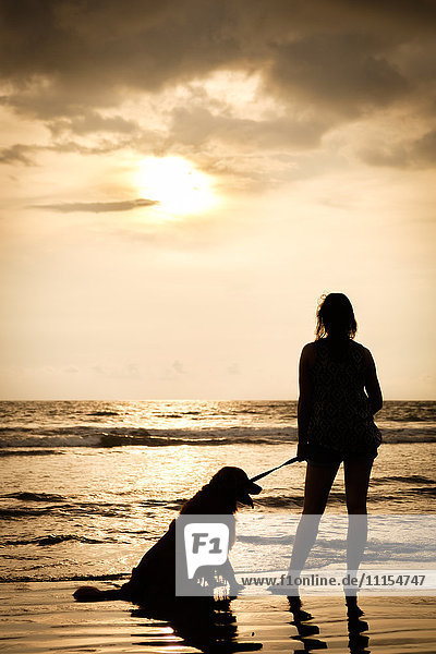 Mexiko  Nayarit  Silhouette einer jungen Frau mit ihrem Hund an der Leine am Strand bei Sonnenuntergang