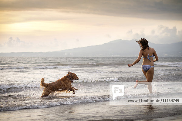 Mexico  Nayarit  Young woman in bikini playing with her Golden Retriever dog at the beach