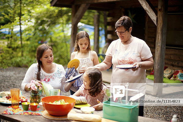 Drei Generationen von kaukasischen Frauen kochen vor der Hütte