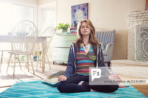 Kaukasische Frau meditiert im Wohnzimmer