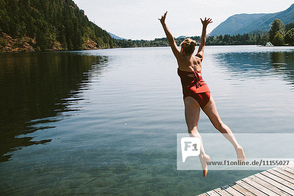 Caucasian woman jumping from dock into rural lake