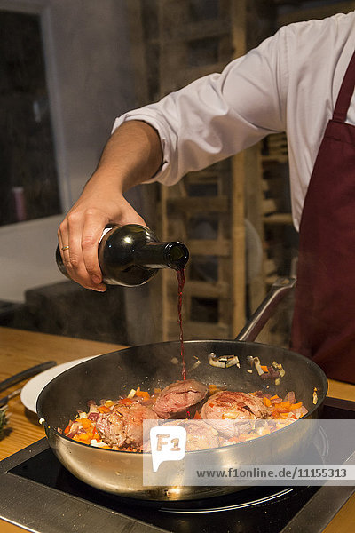 Man pouring wine on beef cheeks in a pan with sauteed vegetables