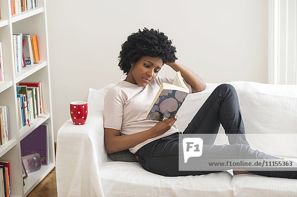 Schwarze Frau liest Buch auf Sofa