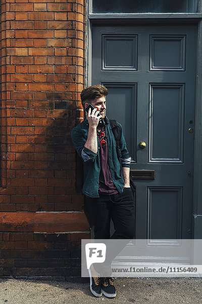 Young man on the phone leaning against entry door