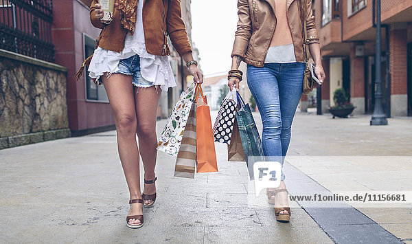 Niedriger Abschnitt von zwei Frauen mit Einkaufstaschen  die in der Stadt spazieren gehen.