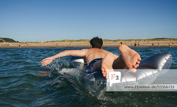 Mann auf Luftmatratze liegend im Meer schwimmend