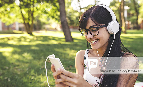 Happy young woman in park listening to music