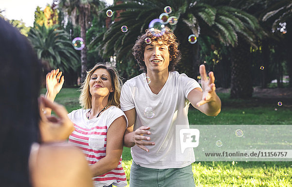 Junge glückliche Freunde beim Spielen mit Seifenblasen im Park