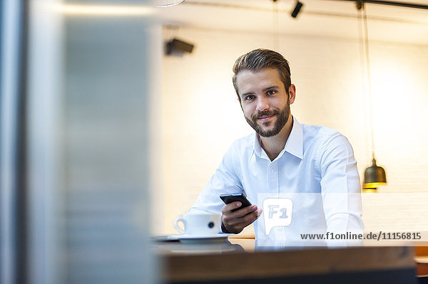 Porträt eines lächelnden Geschäftsmannes mit Handy im Cafe