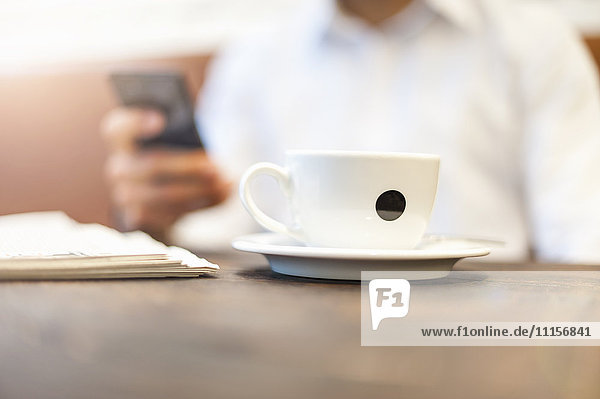 Nahaufnahme von Geschäftsmann Tasse Kaffee mit Geschäftsmann auf Handy im Hintergrund