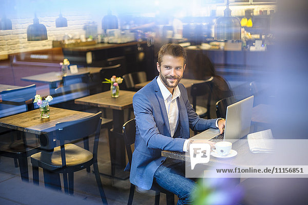 Smiling businessman with laptop in a cafe