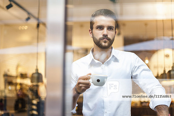 Businessman holding cup of coffee looking through window