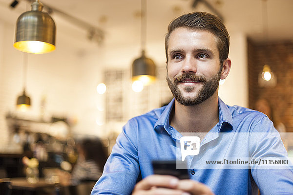 Lächelnder junger Mann mit Handy im Café