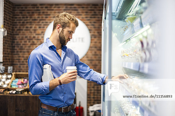 Junger Mann wählt Lebensmittel aus dem Kühlregal eines Coffeeshops aus