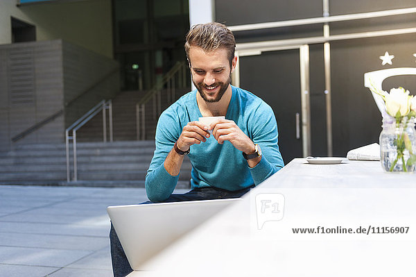 Lächelnder junger Mann auf der Bank sitzend mit Laptop