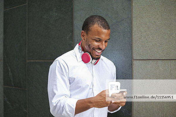 Smiling businessman with headphones looking at smartphone
