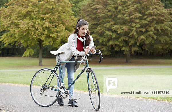 Frau mit Fahrrad in einem herbstlichen Park mit Blick auf das Handy