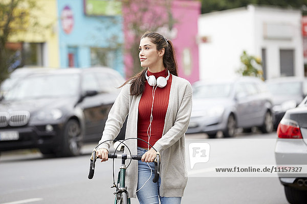 Entspannte Frau mit Kopfhörer und Fahrrad über die Straße