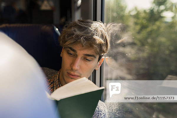 Junger Mann liest Buch im Zug