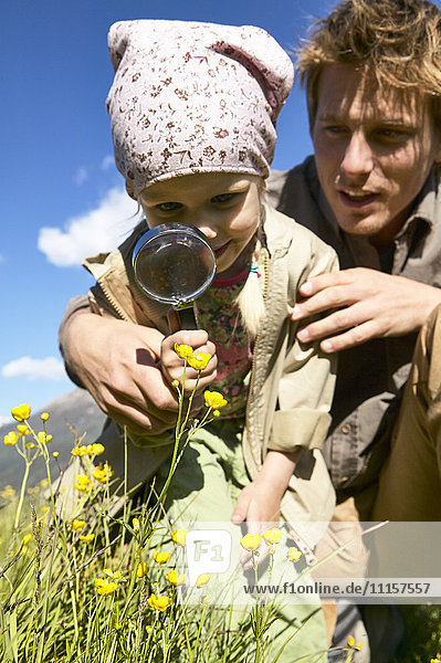 Girl with father examining wild flower with magnifying glass