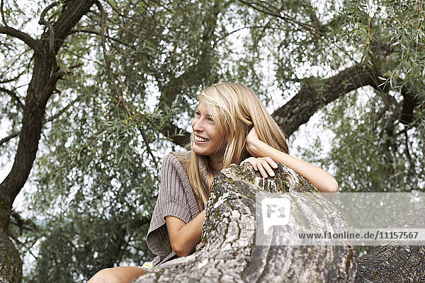 Lächelnde junge Frau an einem Baumstamm lehnend