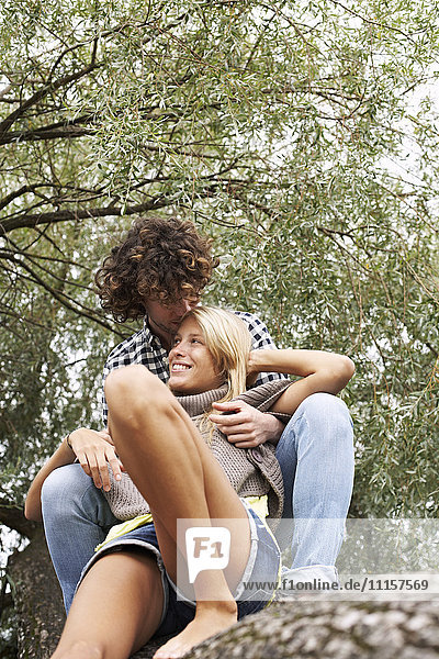 Glückliches junges Paar auf einem Baumstamm sitzend