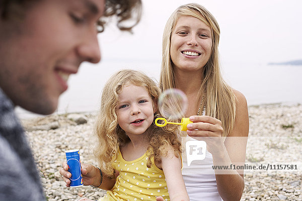 Eltern mit Tochter an einem See  die Seifenblasen bläst.