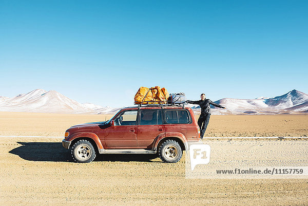 Bolivien  Altiplano  Eduardo Avaroa Andean Fauna National Reserve  Mann hängt an einem 4x4 Auto