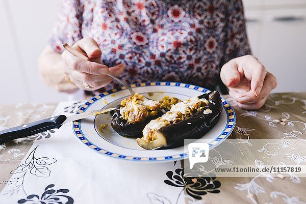 Seniorin beim Essen von gefüllten Auberginen in der Küche  Teilansicht