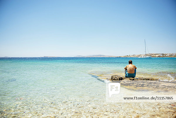 Griechenland  Koufonissi  Mann sitzt auf einem Felsen und schaut auf das klare Wasser der Ägäis.