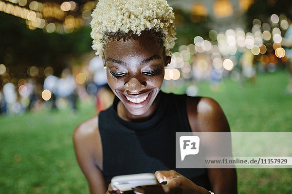 Junge Frau sitzt nachts in einem Park und schaut auf das Handy