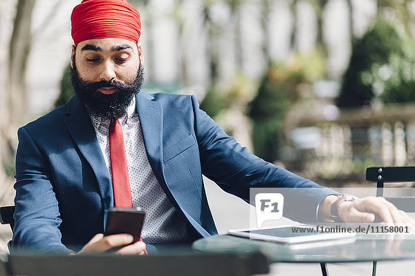 Indischer Geschäftsmann sitzend in Manhattan  mit Smartphone