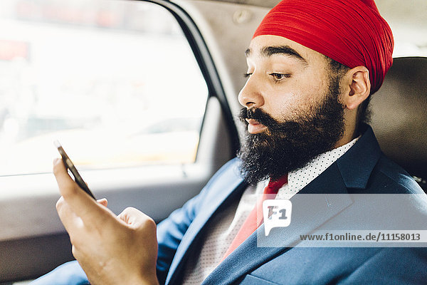 Indischer Geschäftsmann mit Smartphone im Taxi