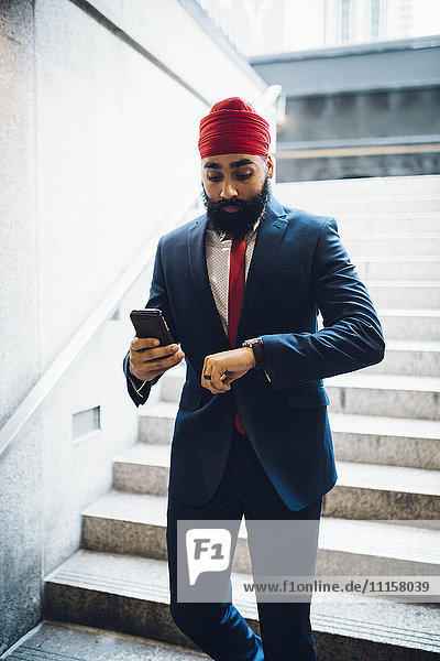Indischer Geschäftsmann geht die Treppe hinunter  schaut auf die Uhr  hält das Smartphone.