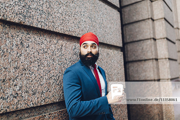 Indischer Geschäftsmann in Manhattan lehnt sich an die Wand und trinkt Kaffee.