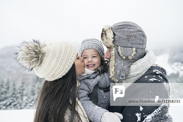Family in winter landscape with mother kissing daughter