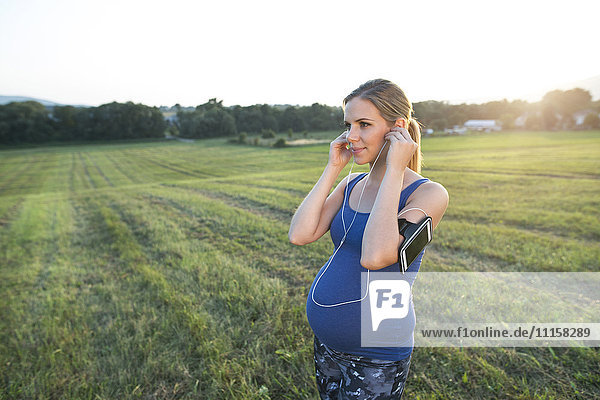 Pregnant woman jogging in field adjusting her earbuds