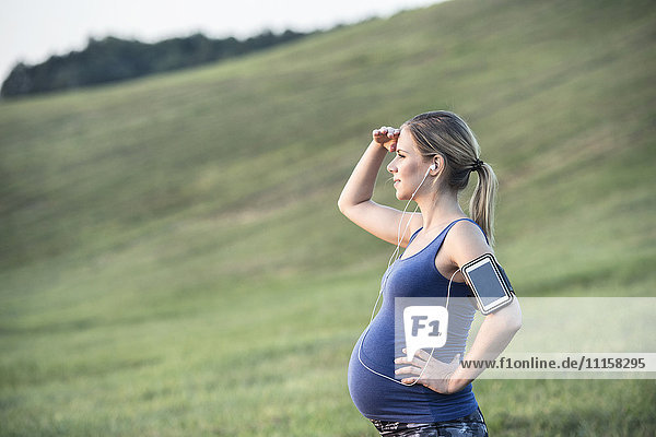 Pregnant woman standing in field taking a break from jogging