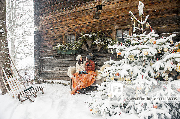 Freunde sitzen auf der Bank am Weihnachtsbaum vor der Berghütte