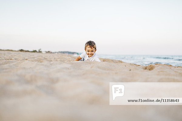Lächelnder kleiner Junge spielt am Strand