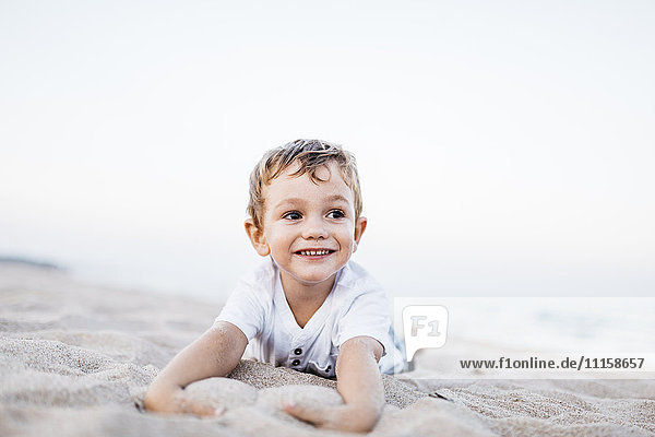 Porträt eines glücklichen kleinen Jungen  der am Strand liegt.