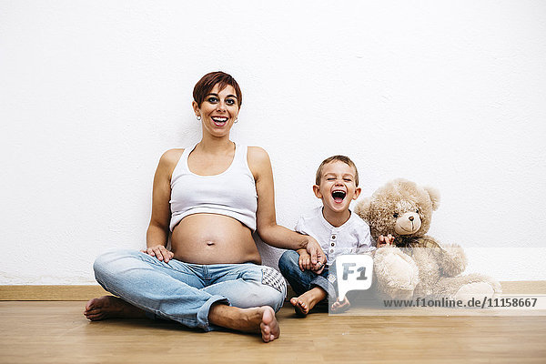Schwangere Mutter und kleiner Sohn auf dem Boden sitzend  lachend