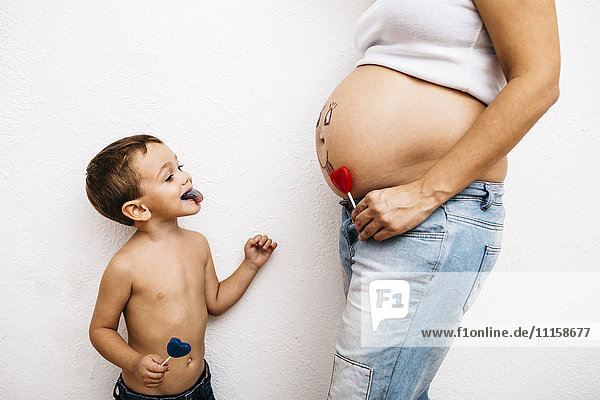 Kleiner Junge  der seine Zunge aus dem Bauch der schwangeren Mutter herausstreckt.