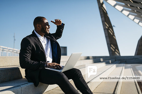 Smiling businessman sitting on stairs using laptop