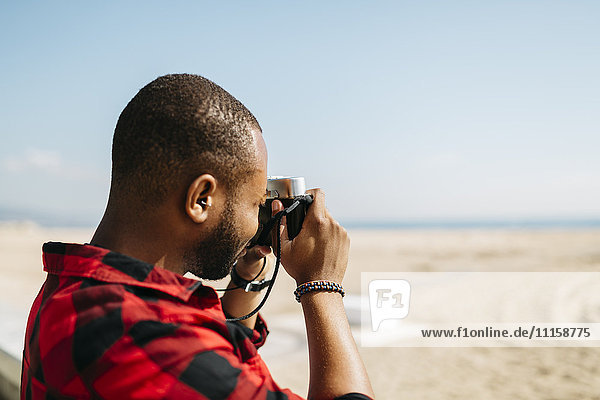 Mann fotografiert mit einer altmodischen Kamera in Strandnähe