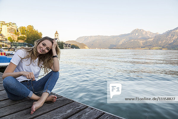 Österreich  Sankt Wolfgang  lächelnde Frau sitzt am Steg am See